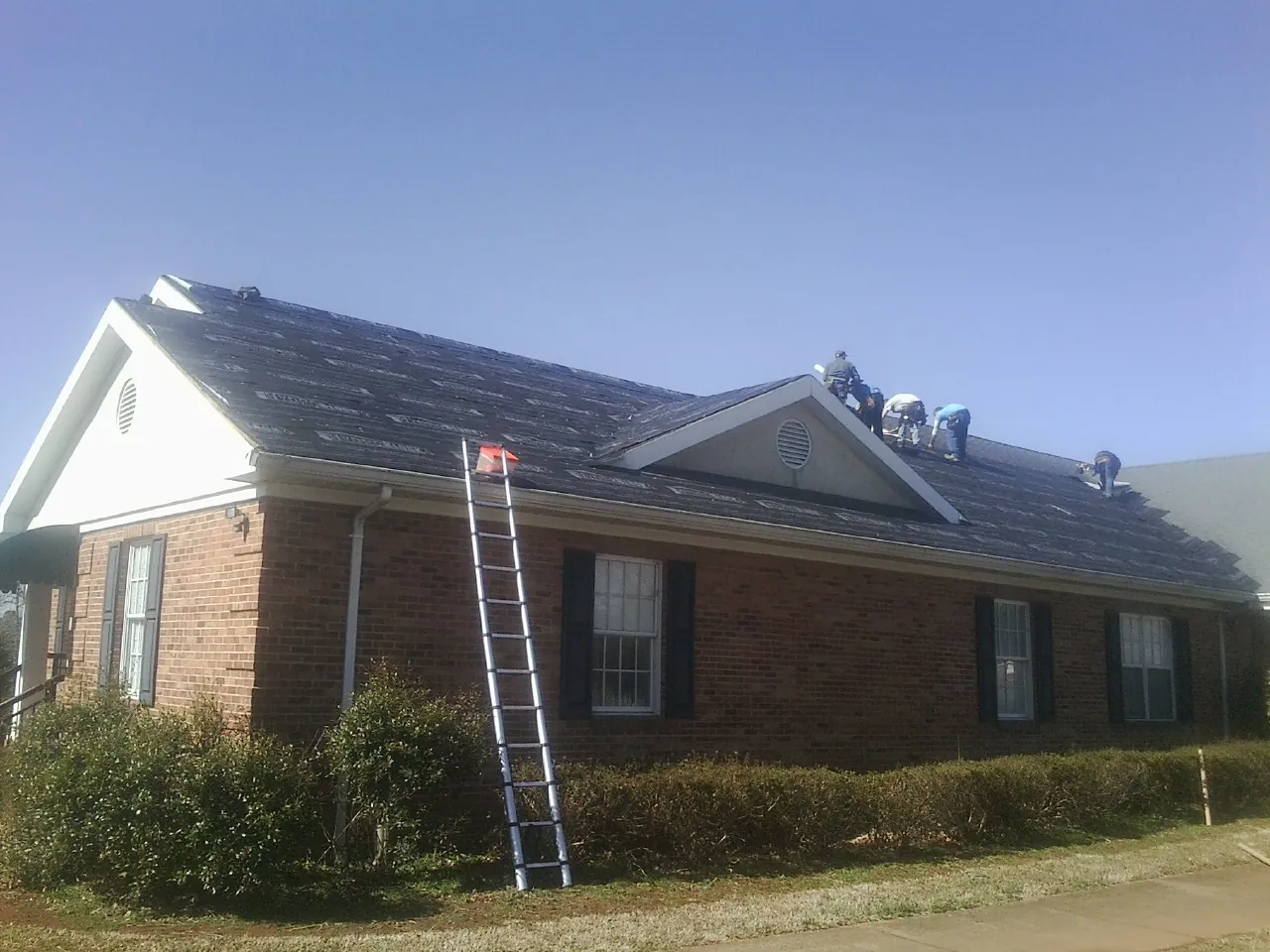 Crew tearing shingles off a brick ranch roof with a ladder set — Emergency Roof Repair work by our crew in Sun River