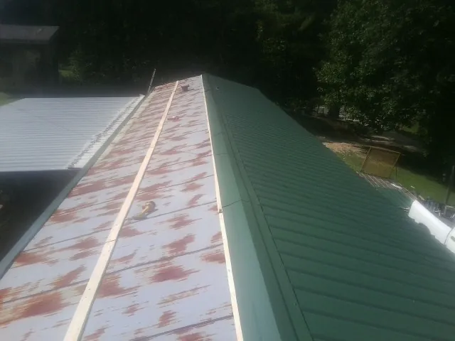 Old rusted panels beside newly installed green metal roofing — Wind Damage Roof Repair by Roofing Brothers in Sun River