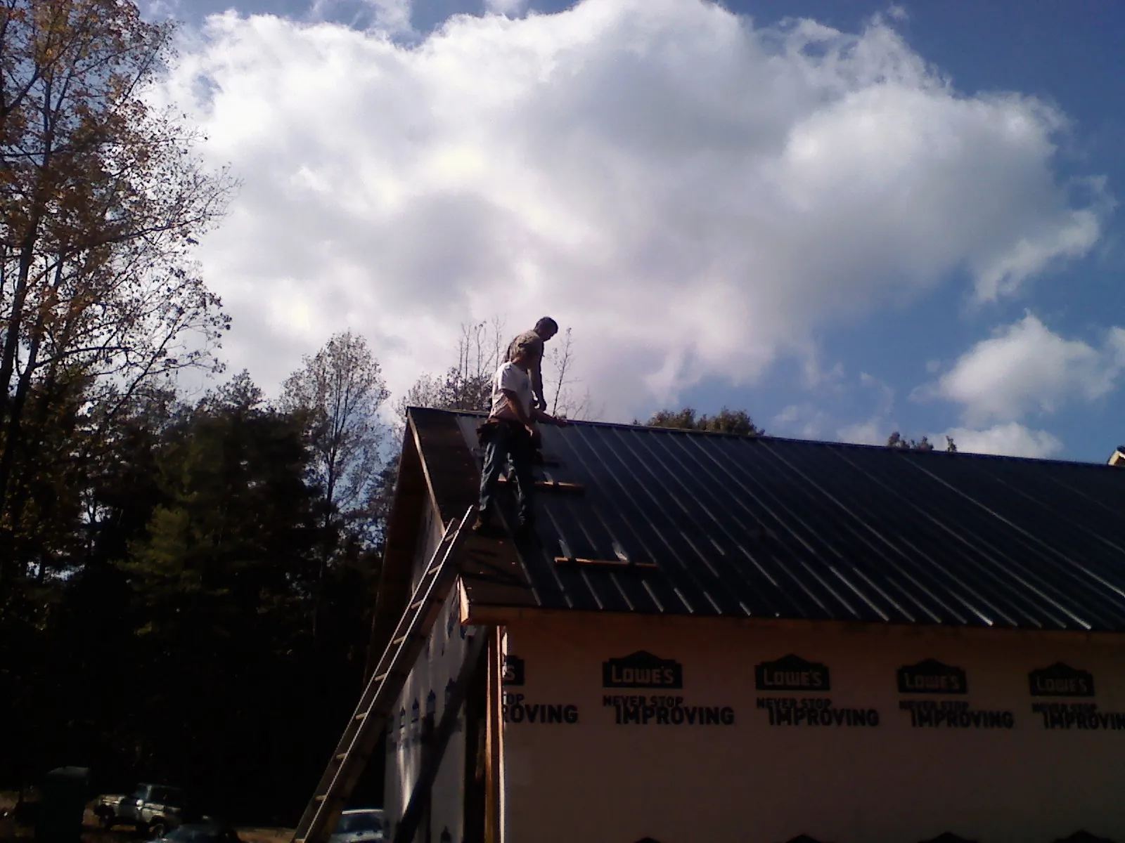 Roofer fastening dark metal panels high against a cloudy sky, from a Roof Inspection job in Sun River