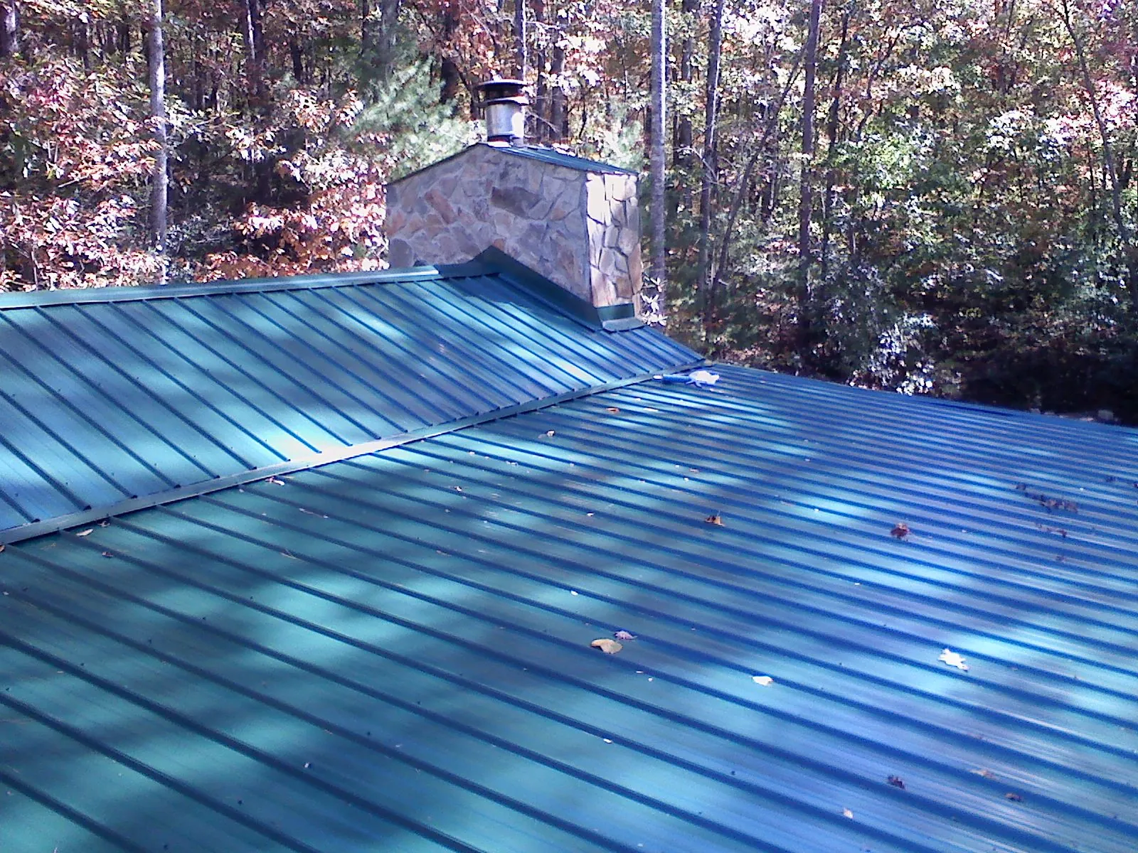 New green metal roof and stone chimney surrounded by autumn woods in Sun River